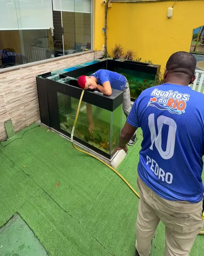 Pedro, da equipe, de uniforme da Aquários do Rio, ao lado do aquário enchendo